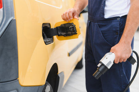 Courier preparing to charge his electric delivery van, holding charging cable and opening socketの写真素材