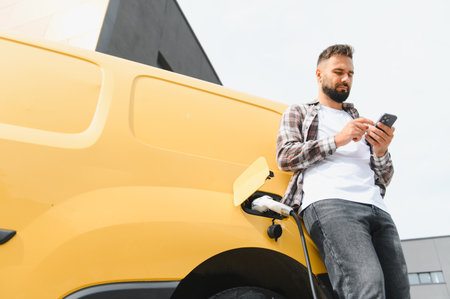 Delivery driver using a smartphone while charging an electric van at a charging station, embracing sustainable transportation and technologyの写真素材