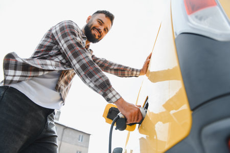 Young adult connecting a power cable to an electric vehicle, embracing a sustainable lifestyle while promoting clean energy and eco friendly livingの写真素材
