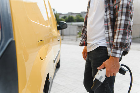 Delivery driver holding a charging cable near his electric van, promoting sustainable transportation and eco friendly delivery servicesの写真素材