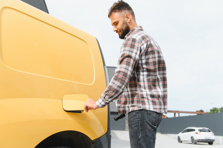 Driver opening the fuel tank cap on a bright yellow van, preparing for a refueling stop in a busy...