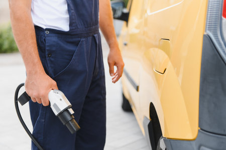 Courier holding a charging cable near an electric van, symbolizing sustainable delivery and eco friendly transportationの写真素材