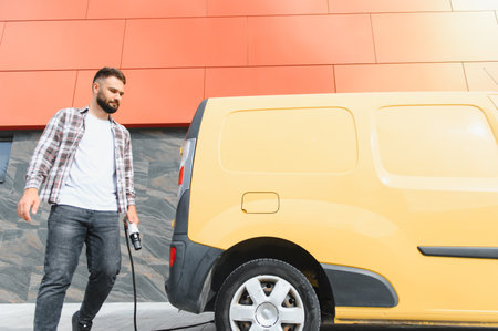Delivery driver charging electric van after completing his delivery round, promoting sustainable...