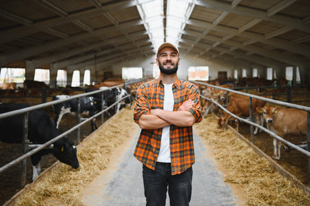 Portrait of a farmer smiling with crossed arms while standing in a cowshed and looking at camera,...