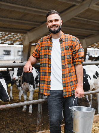 Confident farmer holding metal bucket and smiling in cowshed on dairy farm, taking care of livestock and enjoying agricultural lifestyleの写真素材
