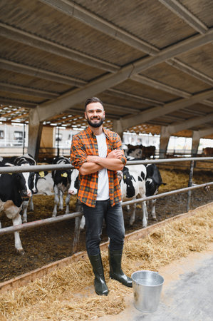 Confident farmer standing with arms crossed in cowshed, representing modern agriculture and livestock managementの写真素材