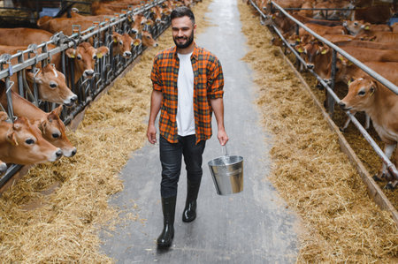 Farmer carrying metal bucket walking through barn and smiling at camera with cows in background...