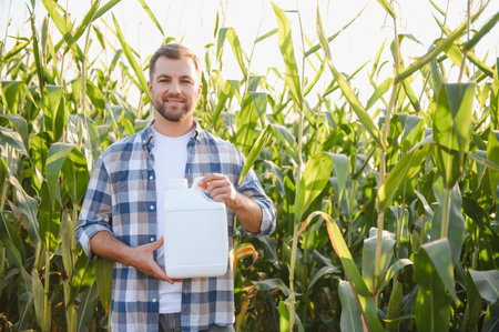 Farmer smiling and holding a white pesticide bottle in a corn field, ensuring crop protection and healthy growthの写真素材