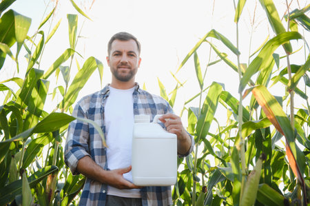 Farmer holding a white pesticide bottle in a corn field, ensuring crop protection and healthy growthの写真素材