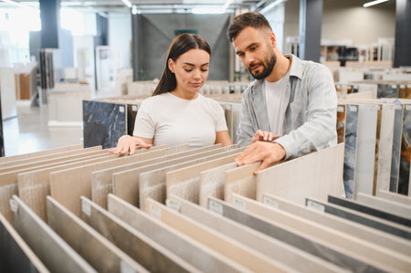 Young couple comparing flooring tile samples in a modern showroom, deciding on materials for home renovation and interior designの写真素材