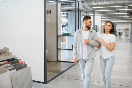Young adult couple selecting new flooring tiles for home improvement project in a modern retail showroom, preparing for house renovationの写真素材