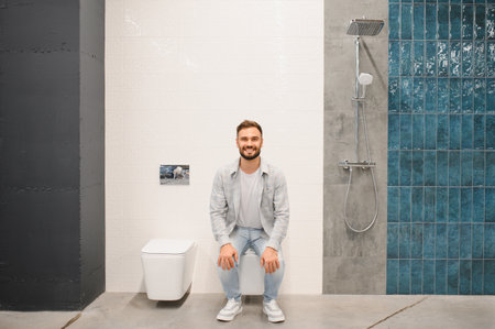 Young man sitting on a toilet in a modern bathroom showroom, choosing new fixtures for home renovation or improvementの写真素材
