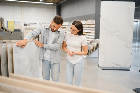 Couple comparing flooring tile samples in a showroom, planning home renovation and choosing materials for their new interior design projectの写真素材