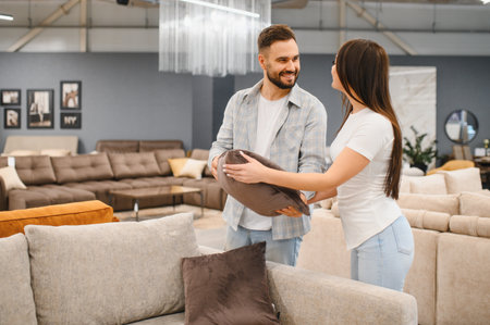 Happy couple shopping for new home furnishings, holding a pillow and smiling in a modern furniture...