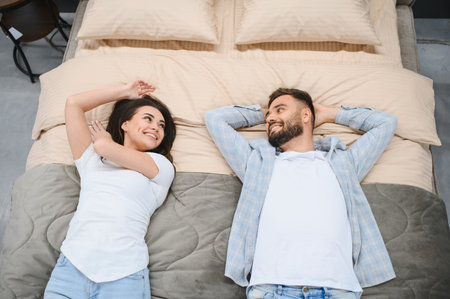 Young couple lying on a showroom bed, smiling and relaxed while testing furniture and choosing pieces for their new homeの写真素材
