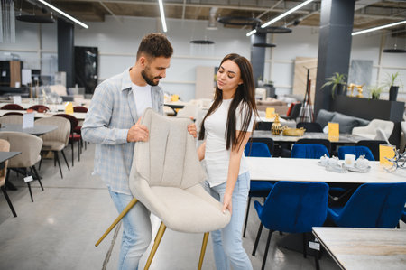 Happy couple shopping for furniture, carrying a modern dining chair in a large furniture store. Buying home decorの写真素材