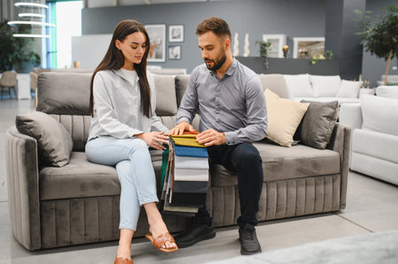 Woman and sales consultant sitting on a modern sofa, choosing fabric samples for home furnishing in a furniture storeの写真素材