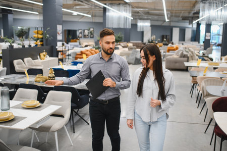 Male salesperson explaining products to a female buyer in a modern retail furniture showroom, offering professional sales assistanceの写真素材