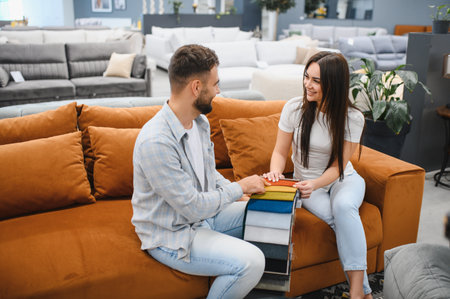 Young couple selecting fabric swatches for a new sofa in a furniture showroom, representing home improvement and interior designの写真素材