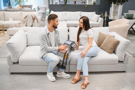Young couple sitting on a sofa, looking at different fabric samples for upholstery, making home decor decisions togetherの写真素材