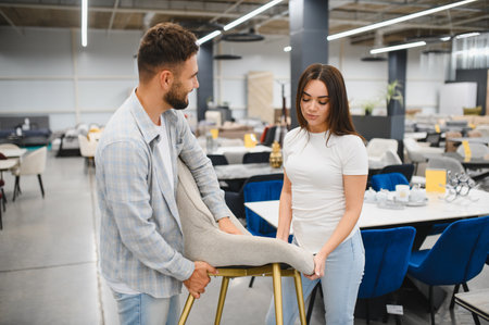 Young couple shopping for household furniture, selecting a new chair for their home. They are holding a modern dining chairの写真素材