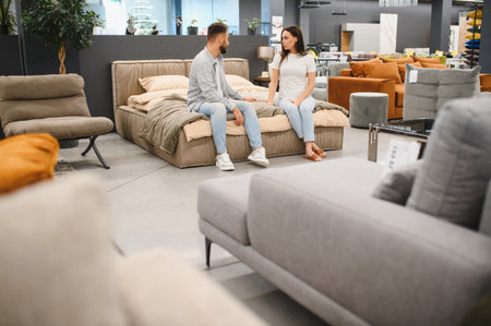 Young adult couple sitting on a bed, discussing and choosing new furniture for their home, shopping in a showroomの写真素材