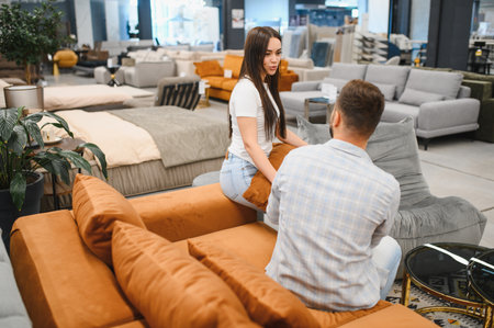 Happy couple in a modern furniture store, sitting on different sofas and talking, making decisions for their new home decorの写真素材