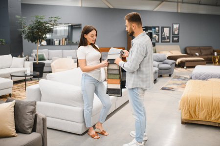 Young couple selecting material from swatches for a new sofa in a modern furniture store, making home decor decisions togetherの写真素材