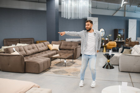 Man in casual outfit confidently pointing at a new sofa display in a furniture showroom while choosing pieces for his homeの写真素材