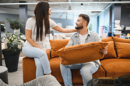 Young couple choosing a sofa for their new home, sitting on furniture and discussing options in a showroomの写真素材