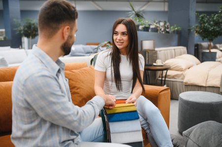 Young couple sitting on a sofa, discussing and selecting fabric samples for new furniture in a modern storeの写真素材