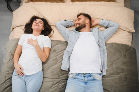 Young couple lying on a new bed, smiling and conversing. Happy people choosing furniture for their...