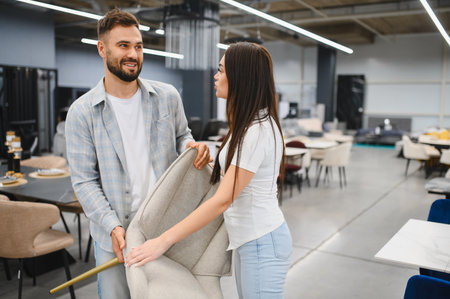 Young couple examining a contemporary chair in a modern furniture showroom, smiling as they choose pieces for their new homeの写真素材