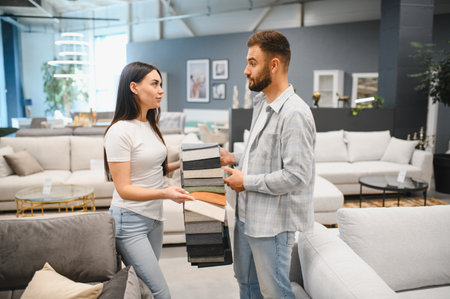Young couple selecting upholstery material swatches for their future living room sofa in a modern furniture showroomの写真素材