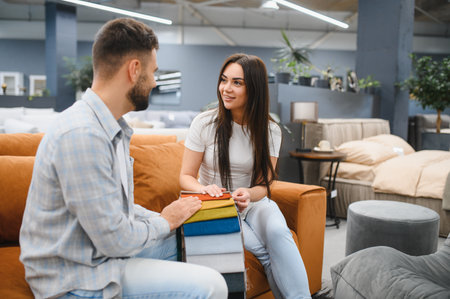 Young couple sitting on a sofa, looking at different fabric samples for upholstery to redecorate their homeの写真素材