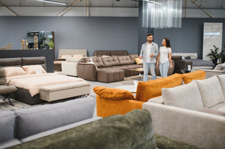 Couple walking through a furniture store showroom, looking for new home decor items like beds, sofas, and other furnishingsの写真素材