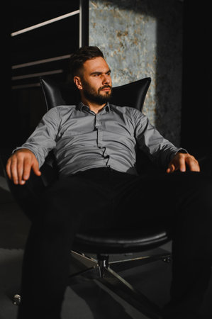 Serious young businessman sitting in black armchair, looking contemplative. Professional with ambitious leadership visionの写真素材