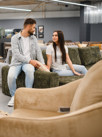 Young couple sitting on a couch, looking at each other while deciding on furniture for their apartmentの写真素材