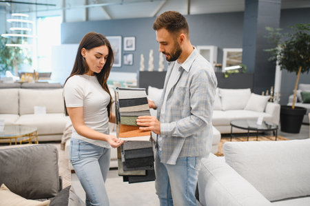Young couple comparing upholstery fabric swatches for their modern living room in a furniture showroom, choosing colors and texturesの写真素材