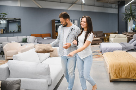 Couple selecting a sofa for their home, holding a cushion and walking through a modern furniture...