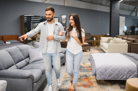 Young couple walking through furniture showroom, man pointing at sofa while woman expresses excitement, shopping for home decorの写真素材