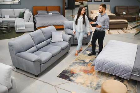 Male sales consultant with digital tablet advising female client comparing sofas and beds in a modern furniture showroomの写真素材