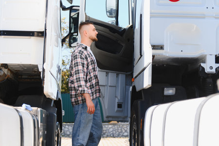 Young male truck driver in plaid shirt standing between two commercial trucks, preparing for logistics operationsの写真素材