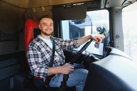 Young confident truck driver in plaid shirt wearing seatbelt, smiling from the heavy truck cabin, ready for long haul transportの写真素材