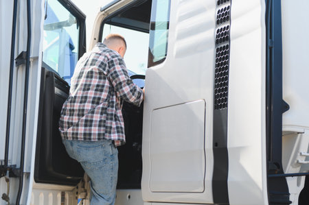 Truck driver in a plaid shirt and jeans getting into the cab of a white semi truck, ready for a freight deliveryの写真素材