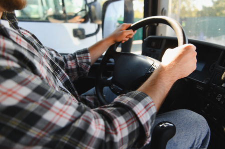 Man in a plaid shirt and beard driving a truck, his hands gripping the steering wheel, transporting goodsの写真素材