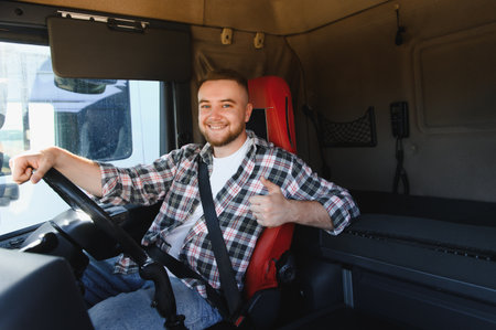 Professional truck driver smiling, wearing a seatbelt, and giving a thumbs up from the semitruck cabinの写真素材