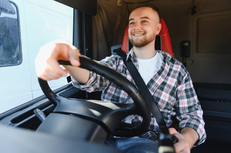 Young man truck driver confidently smiling while navigating heavy transport vehicle, representing...