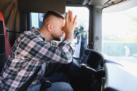 Truck driver feeling stressed and tired, resting head on hands inside vehicle cabin, showing signs of burnout during travelの写真素材