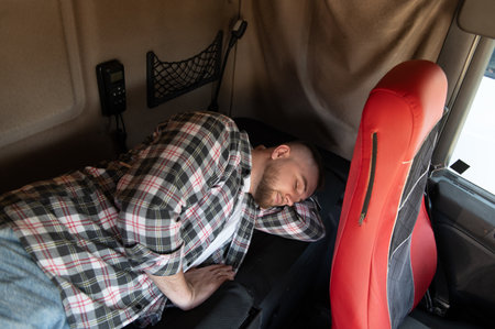 Man sleeping in a truck cabin, taking a break from long haul transport, showing fatigue and rest on the roadの写真素材